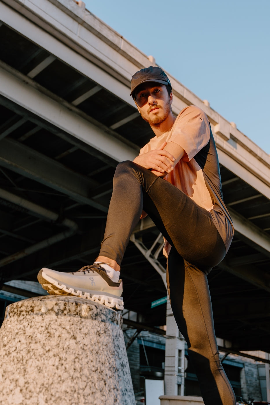 Man posing with his foot resting on top of a pylon. He is wearing black pant and a pair of On Running Shows. 